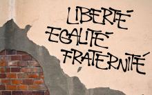 A brick wall is graffitied with the French & Haiti national motto "Liberte Egalite Fraternite", which translates to "Liberty, Equality, Fraternity"