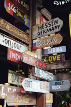 Wooden sign with arrows pointing in multiple directions. Each arrow has a different language or country listed.